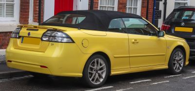 Yellow convertible with black soft top and rear spoiler seen from the back