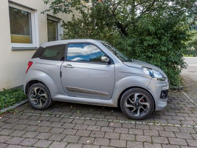 Compact silver microcar with distinctive wheel rims and two-door design