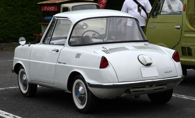Rear view of vintage compact coupe with vented engine cover and round side mirror.