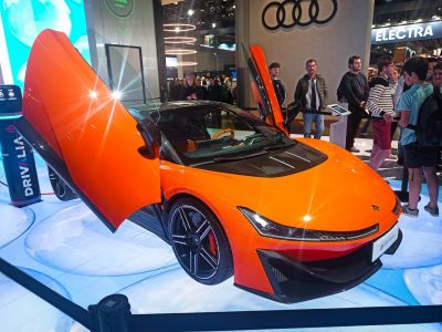 Bright orange sports vehicle with butterfly doors open at an automotive show