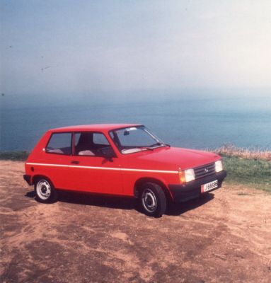 Red compact hatchback with black bumpers and two-door design