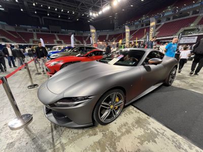 Matte gray sports coupe with aerodynamic hood and alloy wheels at indoor show