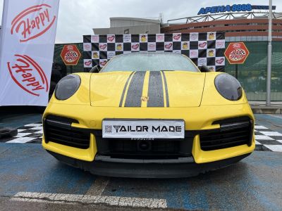 Yellow sports car front view with black racing stripes and rain droplets.