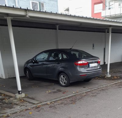 Compact sedan rear side with distinctive taillights under carport