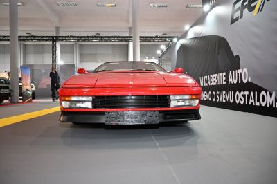 Close-up front of red Ferrari Testarossa with pop-up headlights and grille.