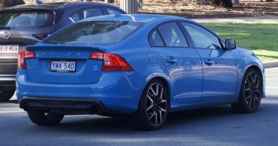 Rear side of blue sedan with tail lights, spoiler, and alloy wheels