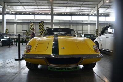 Front view of yellow sports coupe with black racing stripe and pop-up headlights