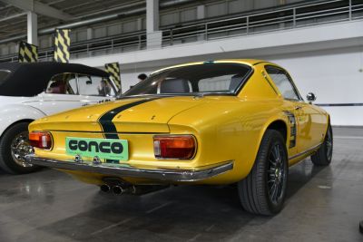 Rear view of a classic yellow racing coupe with dual exhausts and racing stripes