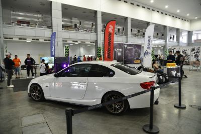 White coupe with bronze aftermarket wheels inside an exhibition area