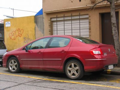 Red sedan side profile with alloy wheels and elongated roofline.