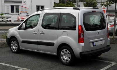 Silver MPV with sliding rear doors and roof rails, side-rear angle.
