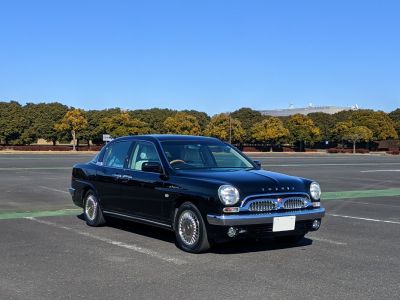 Black sedan with retro chrome grille and round headlights under clear blue sky