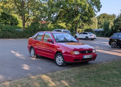 Red sedan with front-side view and classic compact design in urban parking.