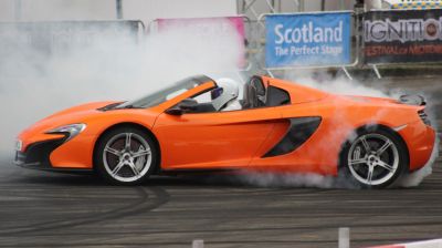 Bright orange open-top sports car performing burnout with tire smoke
