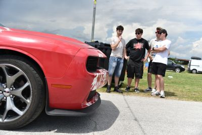 Close-up of red muscle car front, alloy wheels, group of young men outdoors