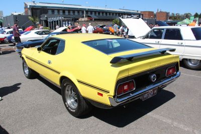 Rear side of yellow classic muscle car with rear spoiler and stripes