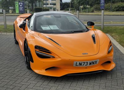 Front view of an orange sports car with aerodynamic vent details and signature headlights.