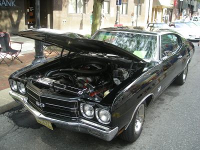 Muscle car with open hood and visible engine, showing front grille and headlights.