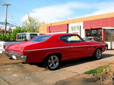 Red 1969 muscle car rear side view with chrome wheels and SS badge