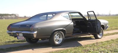 Rear-side view of a classic muscle coupe with open driver door and sporty wheels