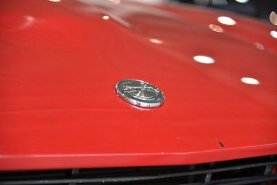 Close-up of a vintage car hood emblem on bright red surface