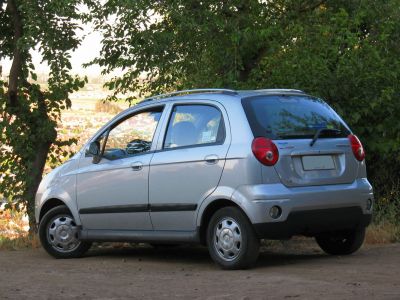 Silver compact hatchback rear side view on dirt road near trees