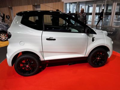 Side profile of compact microcar with black alloy wheels on red floor