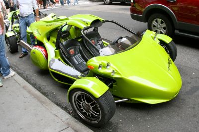 Three-wheeled motorcycle with open cockpit, dual headlights, and exposed suspension