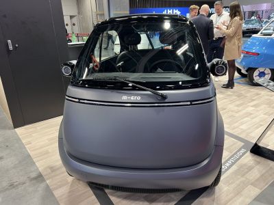 Rounded compact electric microcar front with wide windshield and small mirrors