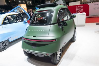 Matte green compact microcar rear with horizontal tail light bar and curved rear window.