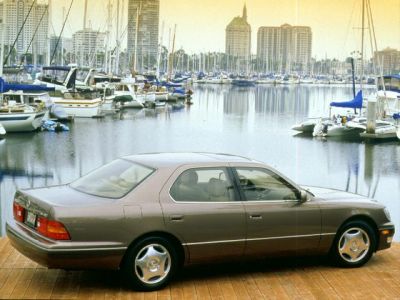 Sedan parked on wooden dock by marina with yachts and waterfront buildings.