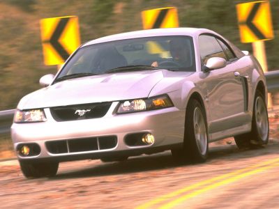 Front view of a silver coupe on a winding road with sharp curve signs