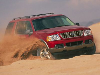 Red SUV driving off-road on desert sand dunes kicking up dust